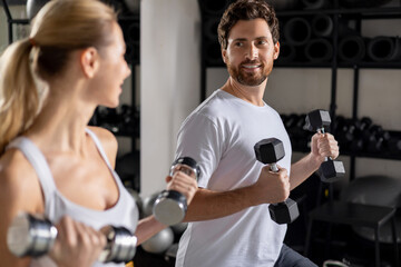 Young man and woman exercising with dumbbells and doing forward lunge