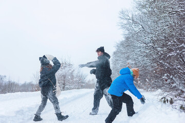 teenager, a young boy, and a girl throwing snow at each other during an outdoor winter game in a snow-covered forest. winter activities, outdoor play, family leisure, and authentic winter moments. 
