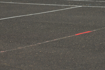 Fototapeta premium asphalt surface with white diagonal line and small red spray mark, shallow depth of field highlights granular tarmac texture, faint chalk