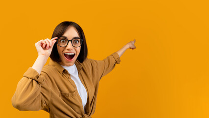 Seasonal sale. Surprised lady pointing at empty space over yellow studio background, banner design,...