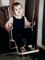 A vintage portrait of a young boy riding on a swing built into a doorway. Photo from 1969.