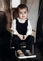 Vintage portrait of a young boy riding on a swing built into a doorway. Photo from 1969.