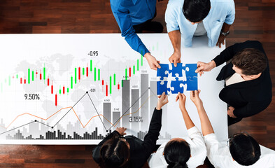 A diverse team collaborates over a table, assembling puzzle pieces and analyzing financial charts to strategize for business growth and successful planning. Scalp