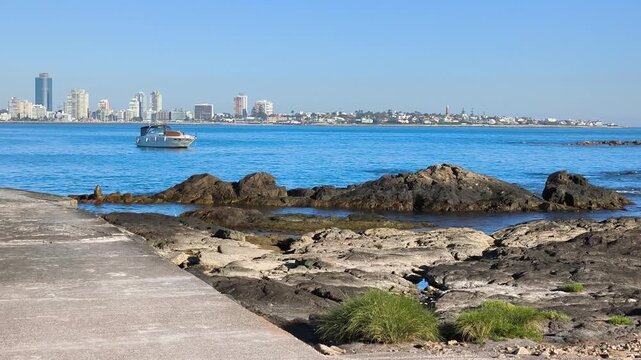 Wide shot from the island shoreline with Punta del Este visible in the distance, sailboats and open sea