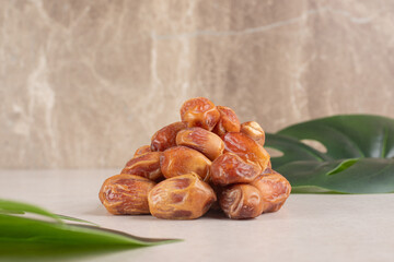 Pile of sweet organic dates on table with green tropical leaf and stone background representing healthy middle eastern snacks and natural energy food