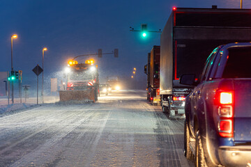 Night winter road scene heavy snowfall snowplow truck clearing icy street, cars freight vehicles waiting green traffic light extreme cold weather conditions. Dangerous urban transport at blizzard