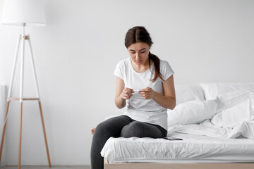 Fototapeta premium Shocked frustrated scared european young female looking at pregnancy test and upset about result, feeling depressed at home alone, free space. Stress, unwanted pregnancy or health problem, infertility