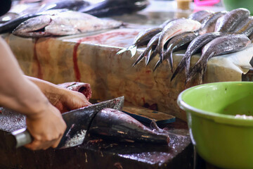 Obraz premium Close up of a fishmonger's hands using a large cleaver to cut fresh tuna on a wooden block at a traditional wet market, capturing authentic local food industry and commerce.