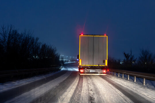 Night winter highway scene freight truck driving icy snow covered road red taillight darkness harsh weather conditions show hard logistics work transport endurance. Cold seasonal industry reality