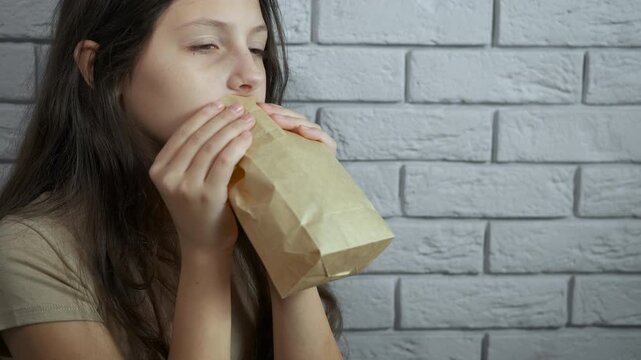 Young girl breathing into paper bag during panic attack. Stressed young girl breathing heavily into a paper bag to calm down during a panic attack, feeling anxious