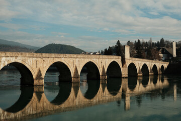 Fototapeta premium Historic Mehmed Pasha Sokolovic Bridge spans the Drina River in Visegrad, Bosnia and Herzegovina. Stone arches and soft reflections highlight the calm atmosphere of this iconic landmark.