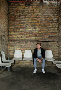 Young man waiting alone in industrial interior with brick wall