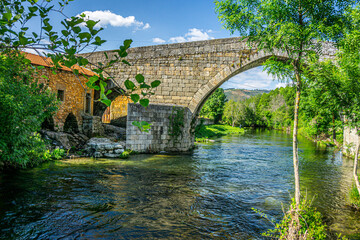 Historic Stone Bridge Over Clear River in Rural Europe.
Old stone bridge crossing a calm river in a green rural European village landscape.