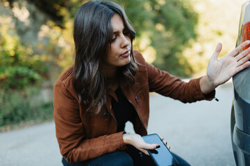 Frustrated young woman looking at scratch on her car