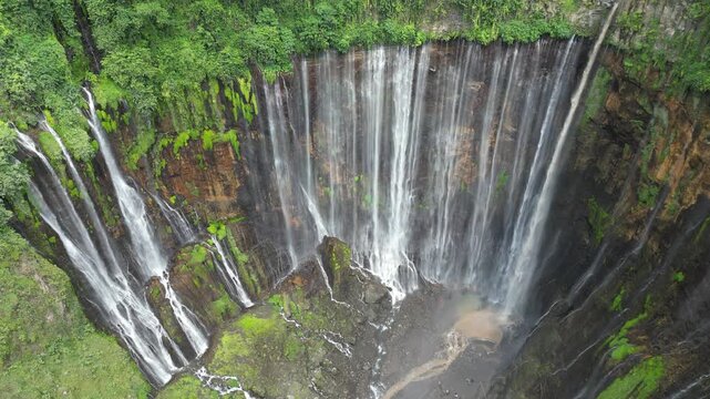 Drone aerial view of Tumpak Sewu Waterfall, East Java, Indonesia. Spectacular dramatic canyon, lush tropical rainforest jungle and majestic volcanic landscape scenery. Famous tourist travel destinatio