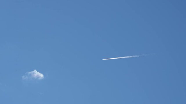 A passenger jet with contrails passing a small cloud