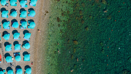 Stunning top-down view of turquoise umbrellas on a pebble beach. Zenithal view of the crystal-clear...