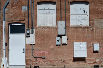 Old brick building with boarded windows and utility boxes on exterior wall, representing aging commercial architecture, property vacancy, and urban infrastructure maintenance