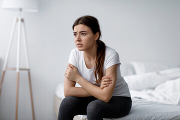Obraz premium Sad anxiety young attractive caucasian woman suffering from mental problems, stress and insomnia sitting on bed alone in bedroom interior, free space. Crisis, trouble, worried, lonely and depression