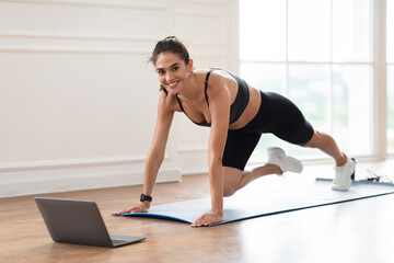 Smiling Sporty Woman Training At Home In Front Of Laptop, Beautiful Female Doing Cross Body Mountain Climbers Exercise Looking At Camera Having Online Video Call With Trainer Instructor
