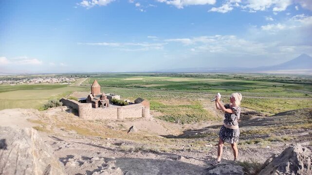 Blonde girl tourist joyfully releasing a white dove against the stunning backdrop of Khor Virap monastery and majestic Mount Ararat, savoring a delightful summer vacation in Armenia. Slow motion