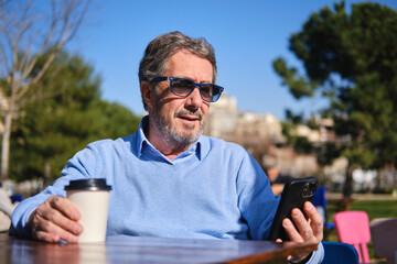 Senior man using smartphone drinking coffee at outdoor cafe