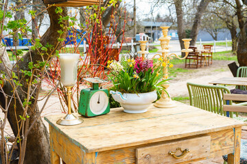 Rustic wooden table decorated with spring flowers, candles and vintage objects in an outdoor garden setting, cafe or flower shop. Cozy countryside atmosphere with seasonal plants and seedlings