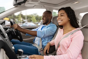 Happy African American man and woman going on summer vacation by car. Beautiful millennial couple sitting inside their new auto, young family cheerfully smiling looking at road, profile side view