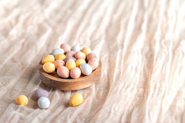 wooden bowl filled with mini eggs on a beige background.