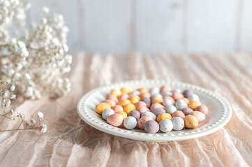 Colorful Easter chocolate eggs in a plate with flowers on a beige background.