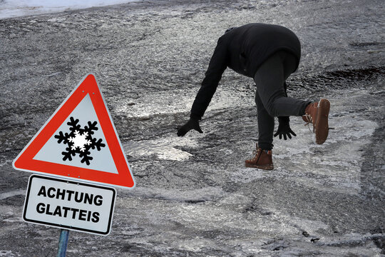 Rutschgefahr auf einem glatten Gehweg im Winter. Eine Frau ist auf dem Eis ausgerutscht. Schild mit Achtung Glatteis 