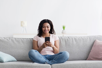 Obraz premium Online chat with tech, meeting, great offer, ad and add, blog in free time, social networks. Cheerful millennial african american lady typing on smartphone or surfing in internet in living room