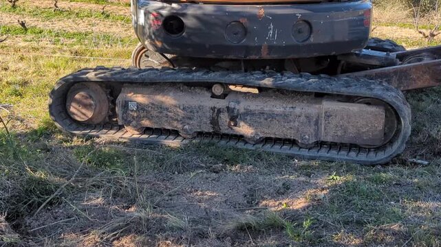 Caterpillar track of a mini backhoe loader filled with dirt moving forward.