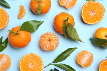 Fresh juicy tangerines and green leaves on light blue background, flat lay