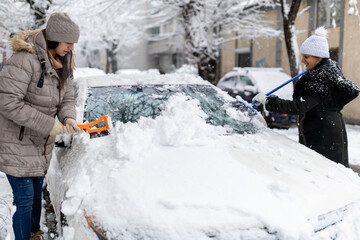 Women clearing snow from car windshield in winter