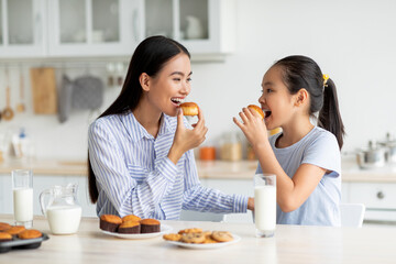 Dessert time for sweet tooth. Happy asian girl and young woman eating cookies and looking at each...