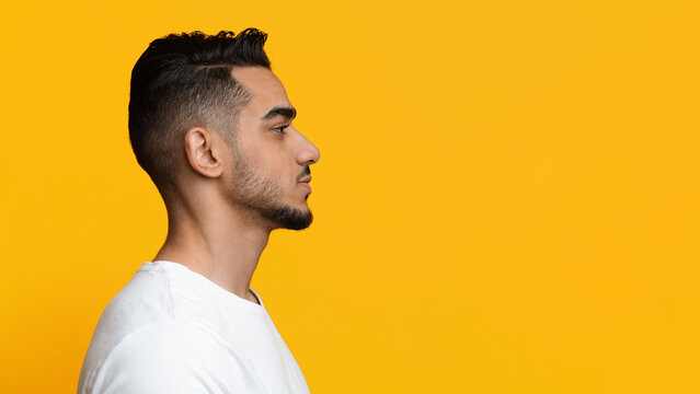 Profile photo of attractive bearded millennial muslim man in white posing on yellow studio background, looking at copy space for your text or advertisement, panorama, closeup