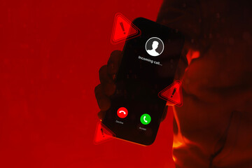 Hand holding smartphone with incoming call screen and warning alert symbols on red background. Concept of phone scam, cyber fraud, identity theft, cybersecurity threat and digital danger.