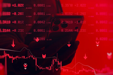 Hand holding smartphone with trading data and falling market charts on red background. Concept of financial crisis, stock market crash, crypto trading loss and investment risk.
