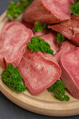 Delicious meat specialties and fine gourmet cuisine.Close-up of sliced boiled veal tongue garnished with fresh herbs. 