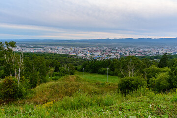Overlooking a sprawling cityscape with lush green hills in the foreground during a calm evening