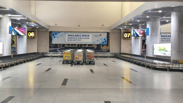 Rows of airport luggage trolleys line the brightly lit terminal corridors, displaying colorful advertising panels and natural light from large glass windows.