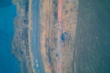 Cyan toxic water and red dirt road contrast, industrial pollution boundary, colorful abstract landscape, aerial drone shot top view
