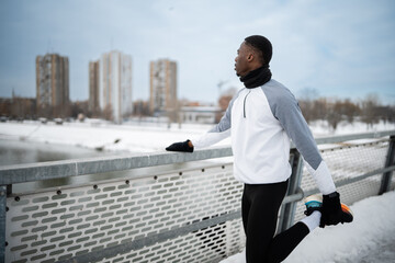 Black man stretching leg on a snowy bridge