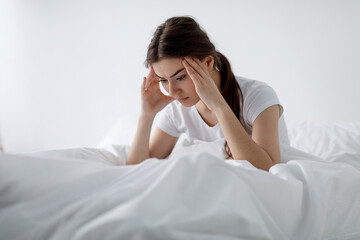 Depressed tired upset millennial attractive european female cant sleep, suffer from headache, stress and insomnia, feeling bad sits on bed, free space. Migraine, bad thoughts, nightmare and crisis