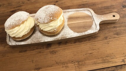 Two Swedish semla buns with whipped cream on rustic wooden board with powdered sugar &ndash; traditional pastries for Fettisdagen (Shrove Tuesday)