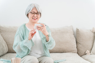 An elderly woman sitting on a sofa and using a smartphone (smile, fun)
