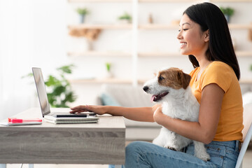 Pretty millennial asian woman in casual freelancer working from home with her cute fluffy doggy,...