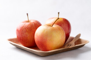 Red apple fruit (Gala apple) in natural plate with wooden fork on white background