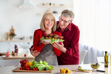 Positive Caucasian senior couple cooking Thanksgiving or Christmas turkey together, preparing...